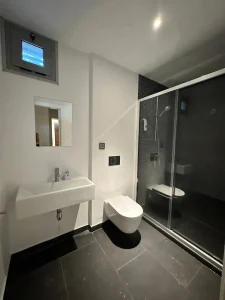 Baño moderno en tonos oscuros con lavabo suspendido, inodoro y ducha acristalada negra.