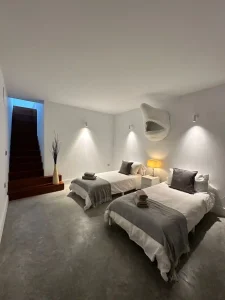 Dormitorio doble con camas individuales, iluminación ambiental en pared y escalera interior al fondo.
