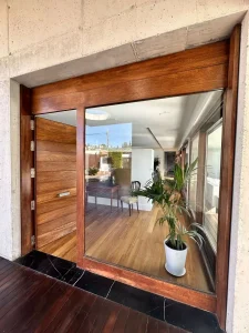 Entrada acristalada con marco de madera que conecta el interior de la vivienda con la terraza exterior.
