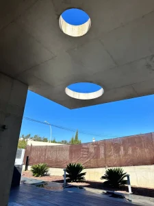 Porche moderno con lucernario circular, techo de hormigón y vista al muro exterior de la villa.