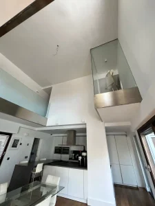 Cocina abierta de techo alto con campana extractora, mobiliario blanco y ventanales laterales.