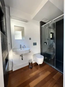 Baño en blanco y negro con lavabo suspendido, inodoro y ducha acristalada de acabado oscuro.
