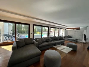 Salón amplio con sofá en L, mesa de centro, grandes ventanales y vistas directas a la piscina.