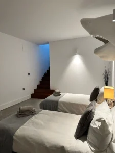 Dormitorio con dos camas individuales, iluminación suave y escalera interior al fondo.