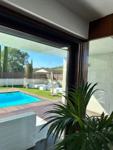 Vista de la piscina y terraza exterior desde una estancia interior acristalada de la villa.