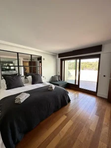 Dormitorio principal con cama doble, textiles oscuros, suelo de madera y salida directa a la terraza.