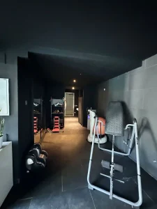 Gimnasio privado con máquinas de entrenamiento, pesas y ambiente oscuro contemporáneo.