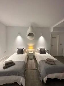 Dormitorio doble simétrico con dos camas individuales, lámpara central y mesita entre camas.